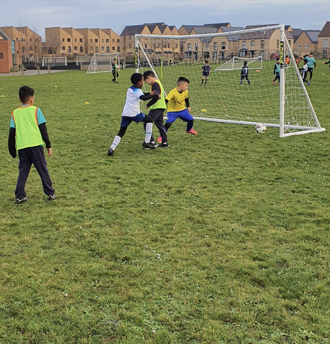 Children playing a football match on the field at The Pathfinder Primary School